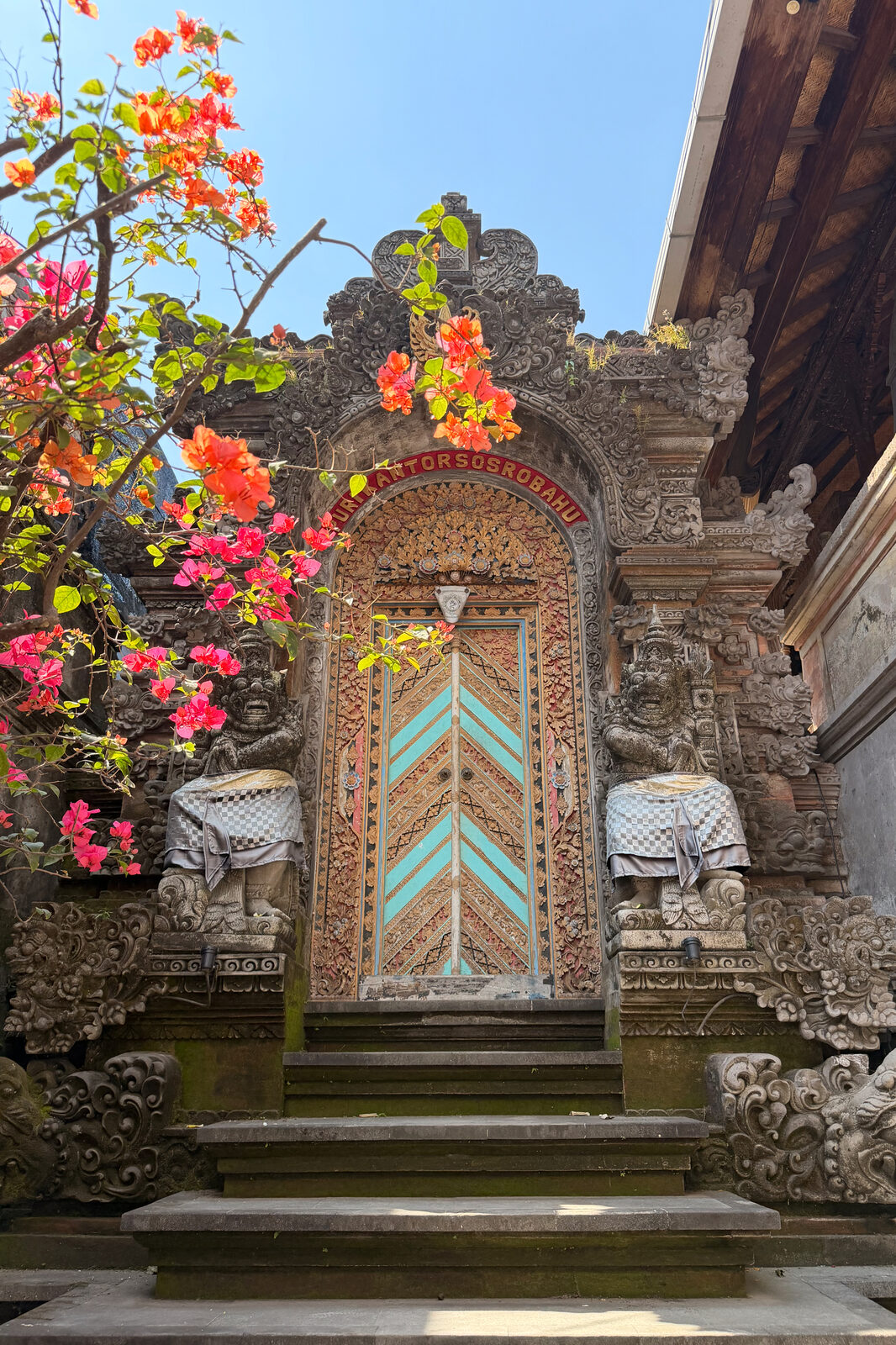 A gate with a blue and gold door under bougainvillea.