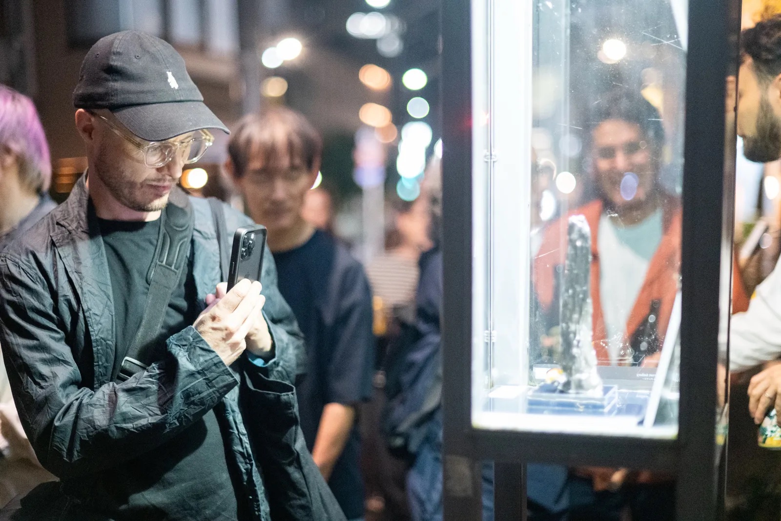 A visitor photographing an artwork inside a Jinny Street Gallery streetlamp at night.